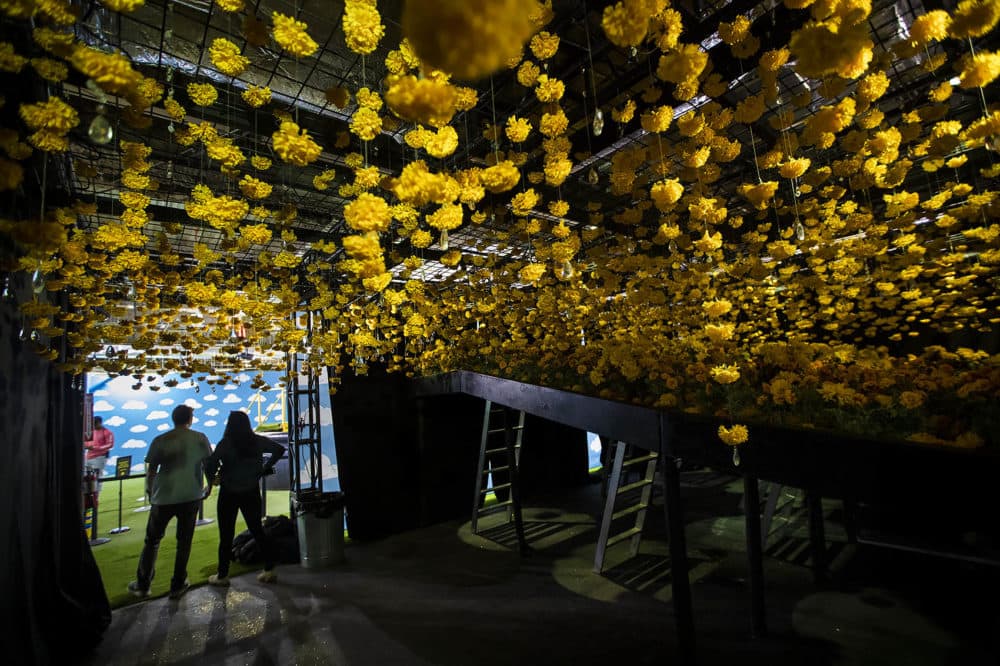 Riley Bates and Madison Munoz walk out of a room with hundreds yellow carnations hanging from the ceiling at “Happy Place.” (Jesse Costa/WBUR)
