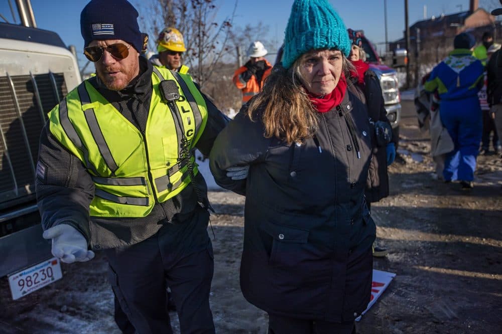 Weymouth Police escort Lisa Jennings away from the natural gas compressor site as she is one of four people arrested for obstructing a truck from leaving the compressor building site. on the Fore River (Jesse Costa/WBUR)