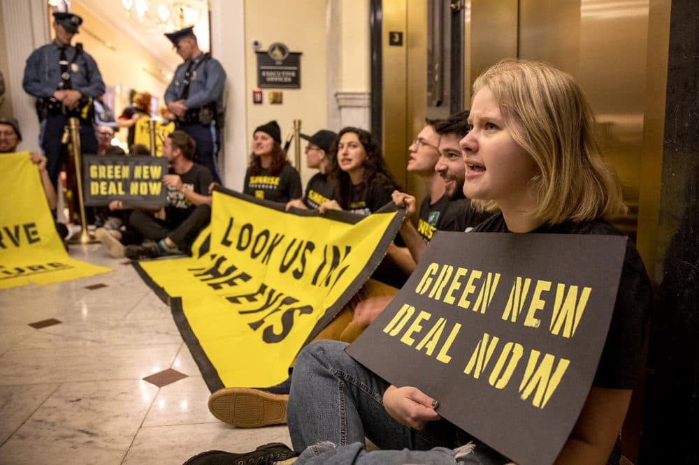 Adele Andrews, who studies at Northeastern University, holds a banner demanding a Green New Deal. Andrews and several other protesters were sitting outside Baker's office. (Robin Lubbock/WBUR)