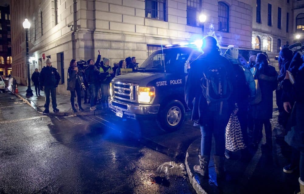 Outside the State House climate activists continue to sing protest songs, as arrested protesters are taken away in a State Police van. (Robin Lubbock/WBUR)