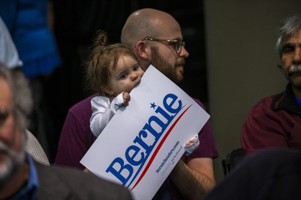 13-month-old Eliza Bugg chews on a Bernie Sanders sign while she and her father, Aaron, wait for his arrival at a campaign event at Simpson College in Indianola, Iowa. (Jesse Costa/WBUR)
