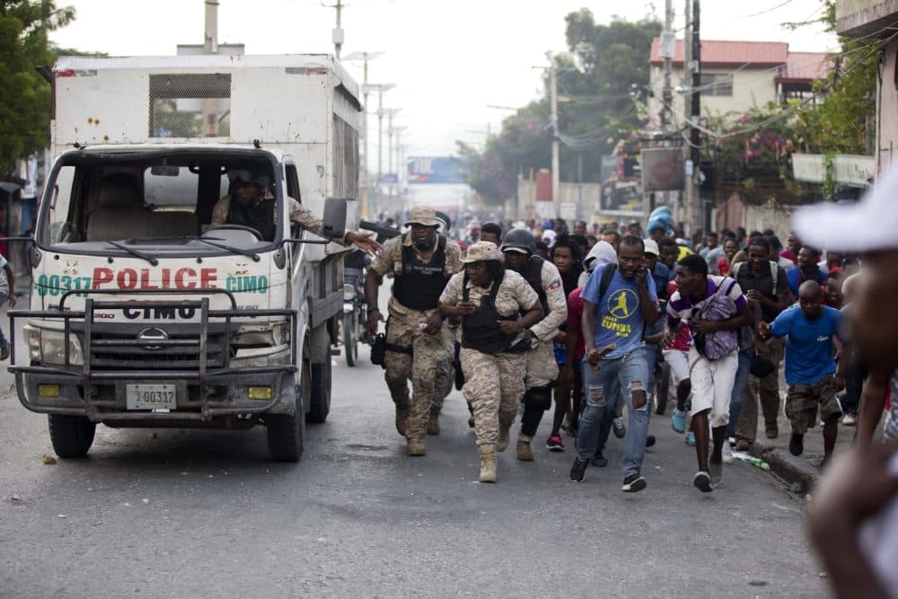 Police officers and protesters take cover behind a police truck as shots ring out during a protest to demand the resignation of Haiti's president Jovenel Moise in Port-au-Prince, Haiti, in November (Dieu Nalio Chery/AP)