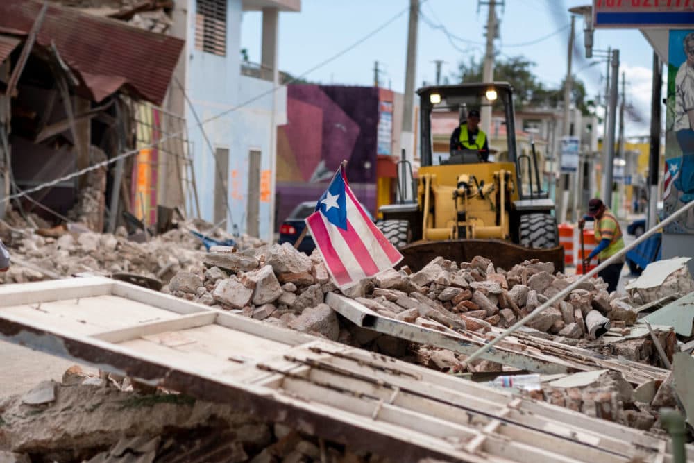 A Puerto Rican flag waves on top of a pile of rubble as debris is removed from a main road in Guanica, Puerto Rico on January 8, 2020, one day after the earthquake. (Ricardo Arduengo/AFP/Getty Images)