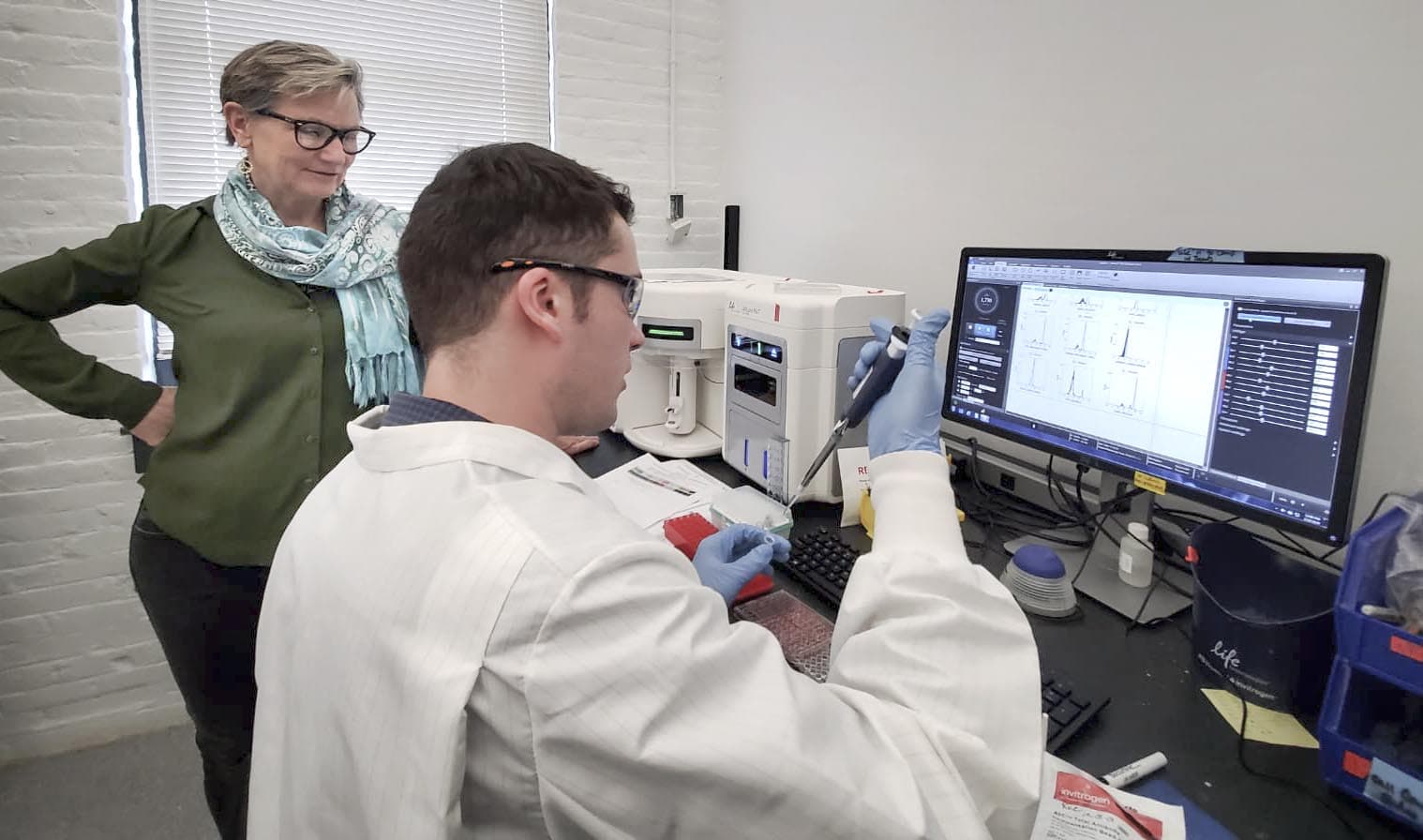 Anne De Groot speaking with a lab scientist at EpiVax. (Angus Chen/WBUR)