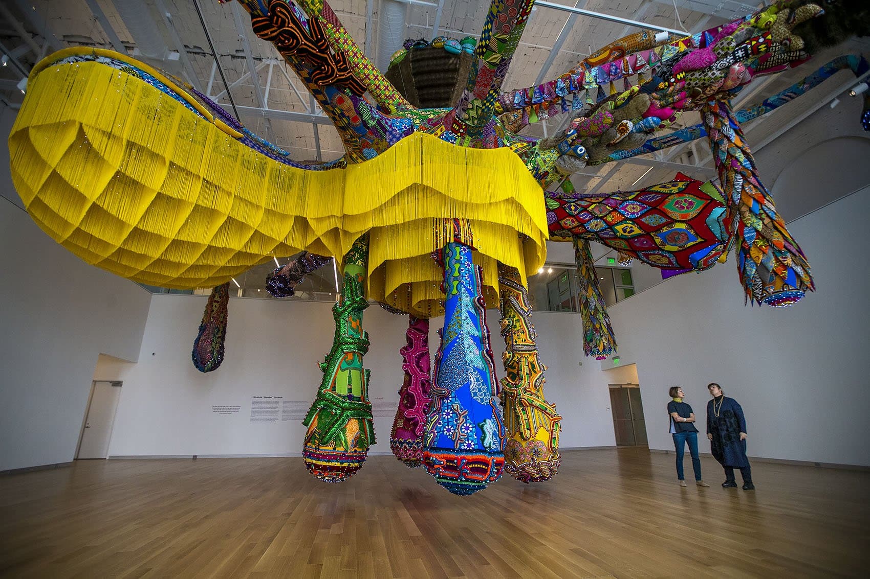 Lisa Tung, executive director and curator at MAAM, left, speaks with artist Joana Vasconcelos beneath her piece, "Valkyrie Mumbet." (Jesse Costa/WBUR)