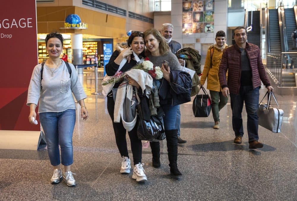 Lina Issa hugs her sister-in-law Ikhlaas Afraam, as they walk with their families through Logan Airport. (Robin Lubbock/WBUR)