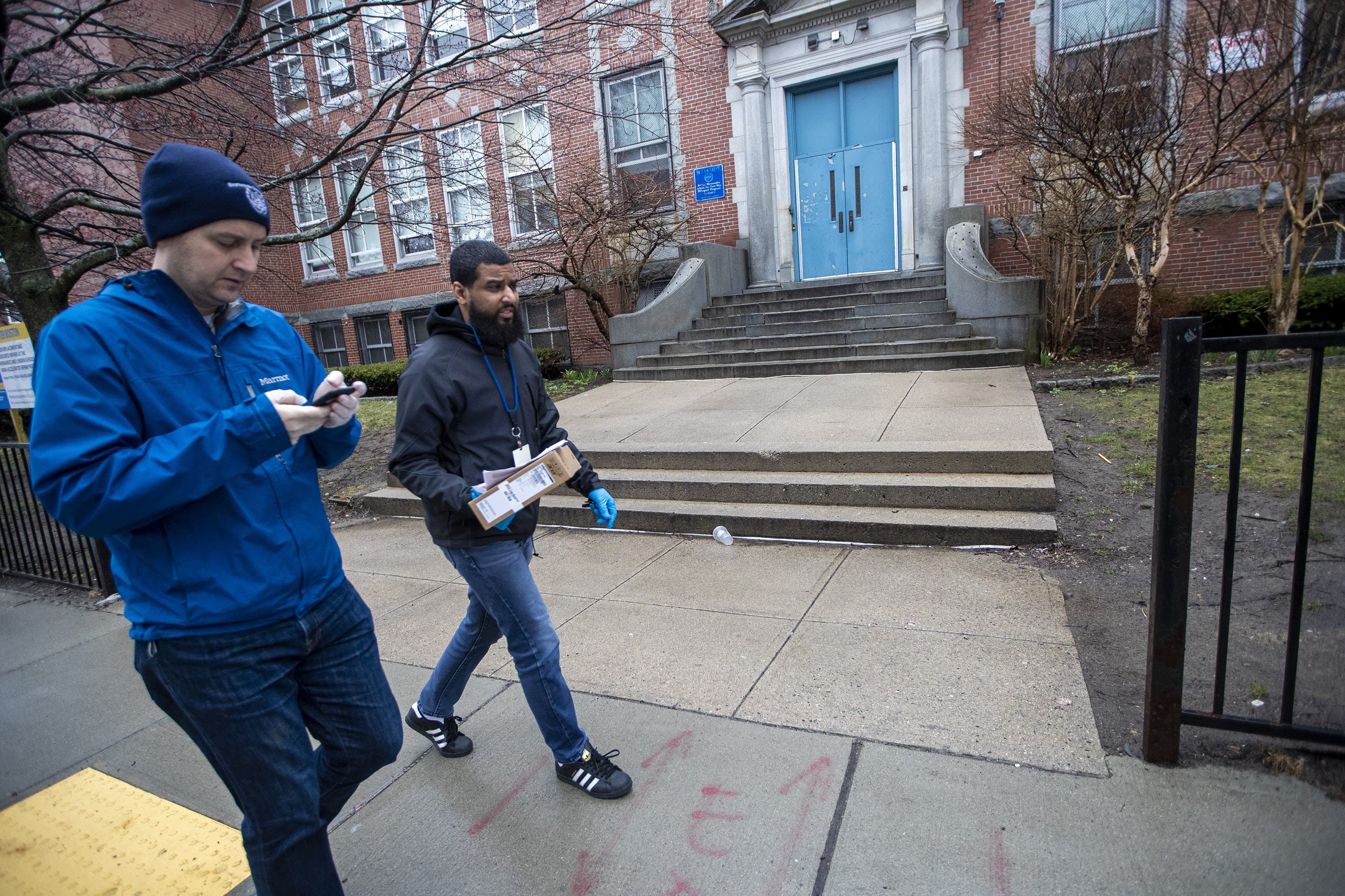 Mark Racine, Director of Development at BPS, and Giscar Centeio walk past the Rafael Hernandez K-8 Elementary School enroute to deliver a Chromebook to a student in Roxbury. (Jesse Costa/WBUR)