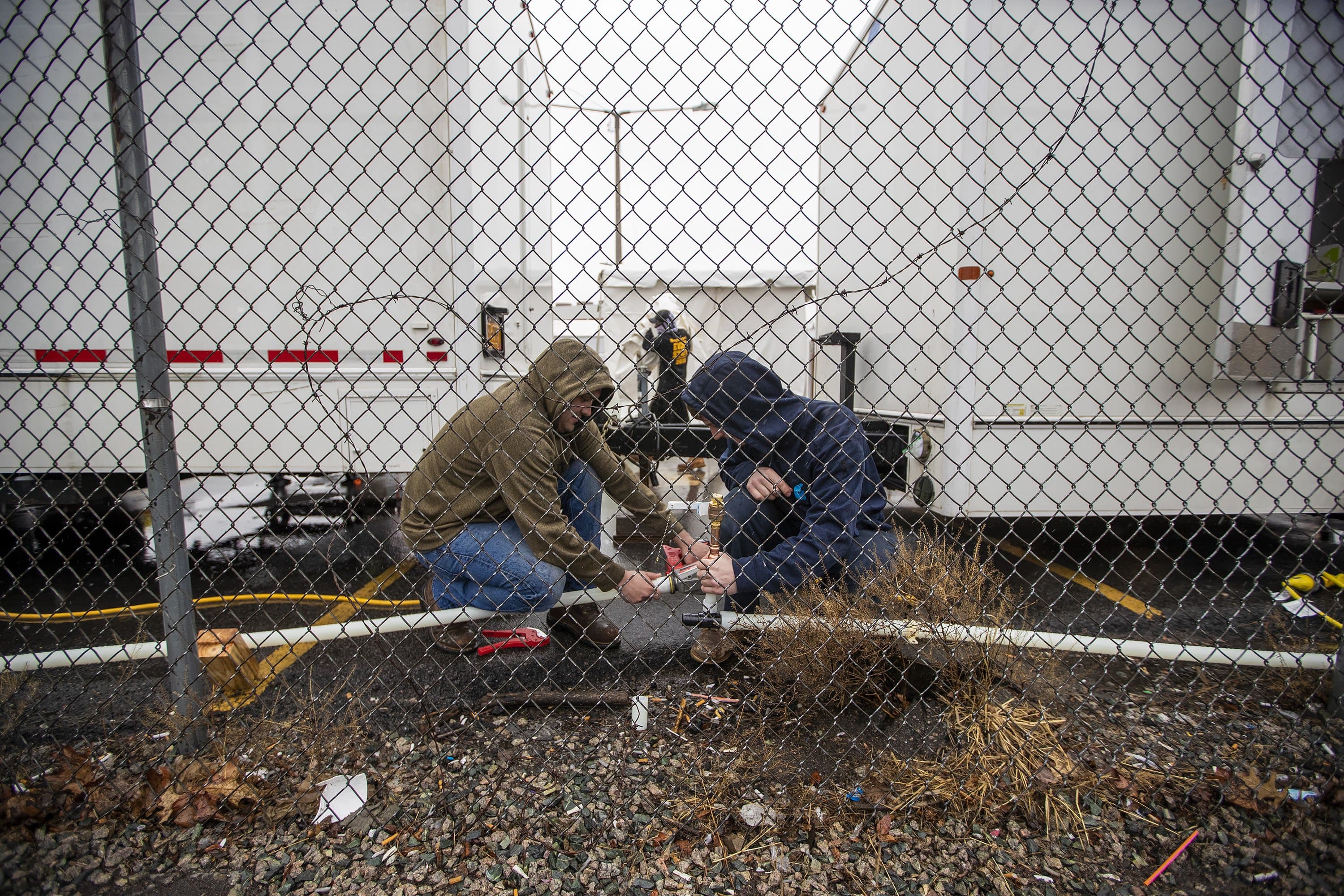 Two contractors work on plumbing for water distribution during construction of Coronavirus testing tent for homeless behind the shelter on Southampton St. in Boston. (Jesse Costa/WBUR)