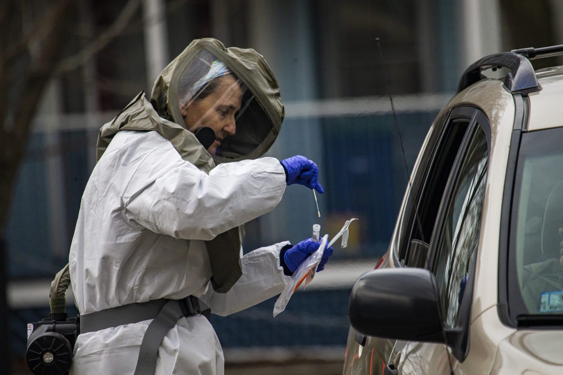 March 22: A health care worker places a cotton swab into a vile after taking a sample from someone being tested for COVID-19 at a drive-thru testing area at Somerville Hospital. (Jesse Costa/WBUR)