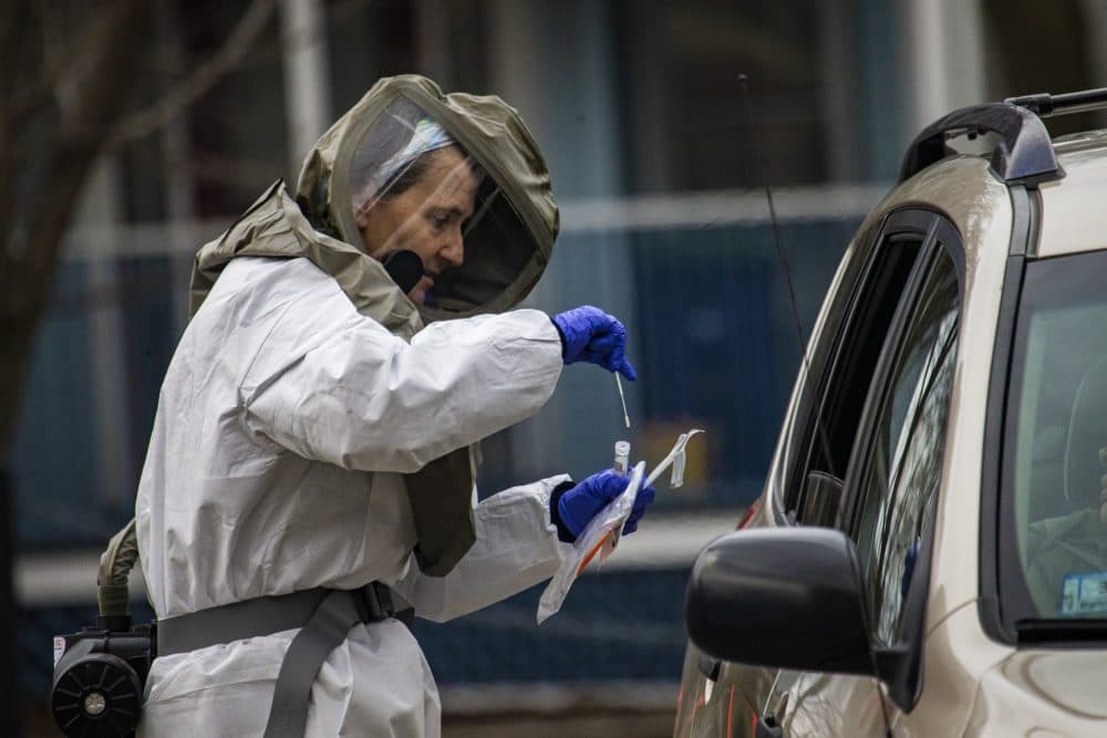 A health care worker in a haz-mat suit places a cotton swab into a vile after taking the sample from someone being tested for COVID-19 at a drive-thru testing area at Somerville Hospital. (Jesse Costa/WBUR)