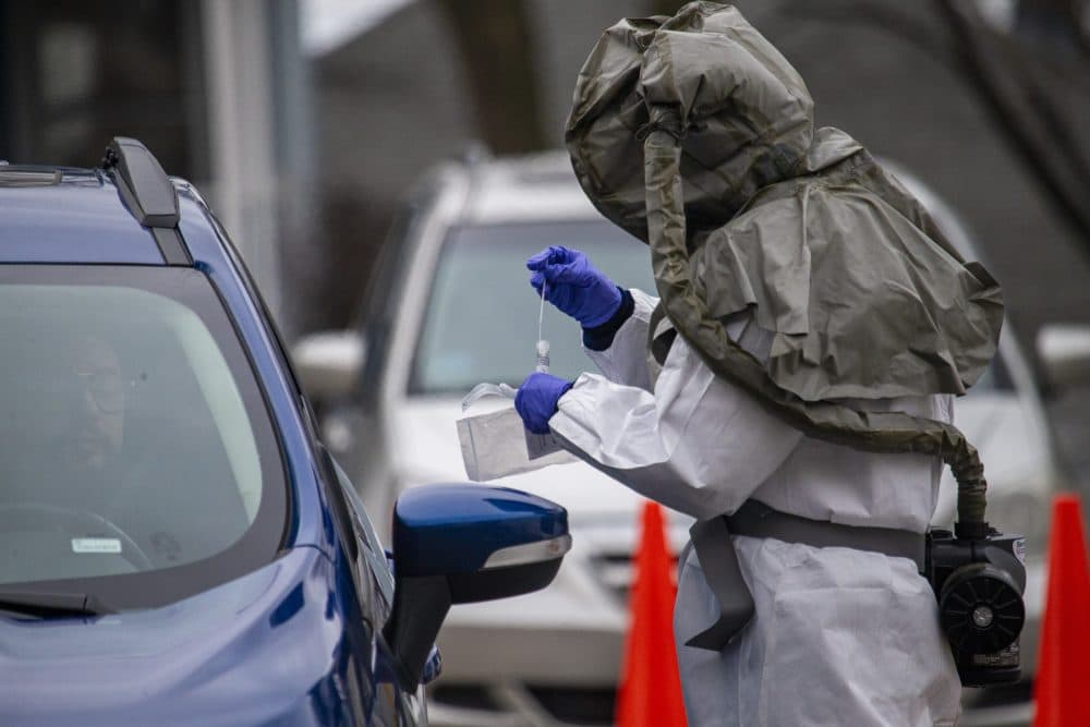 A health care worker places a cotton swab into a vial after taking it from someone being tested for COVID-19 at a drive-through testing area at Somerville Hospital. (Jesse Costa/WBUR)