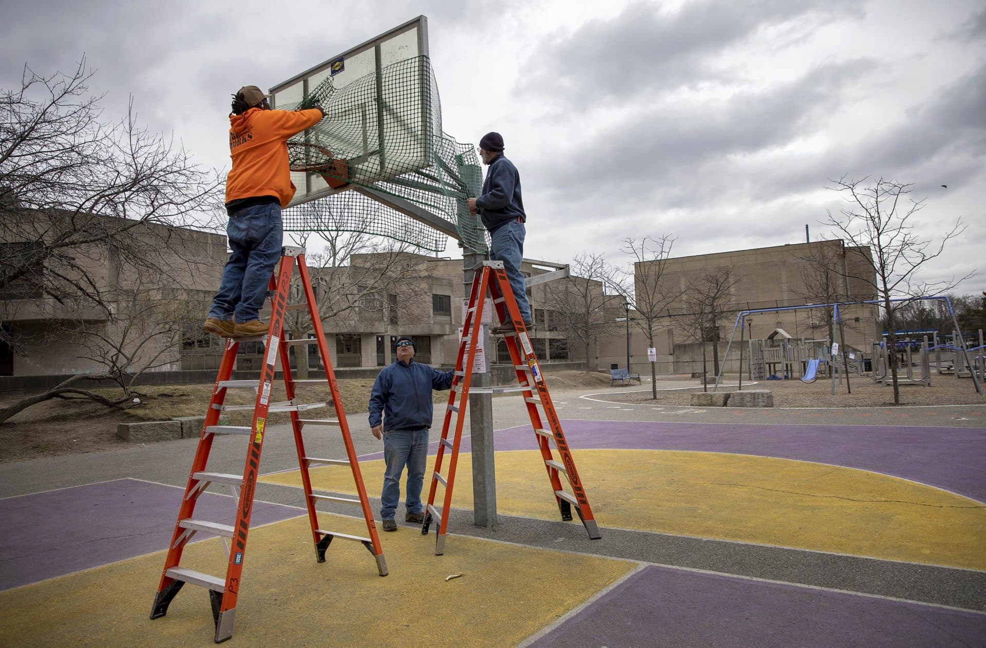 March 23: Cambridge Department of Public Works staff wrap a basketball hoop in plastic fencing to discourage team games. (Robin Lubbock/WBUR)