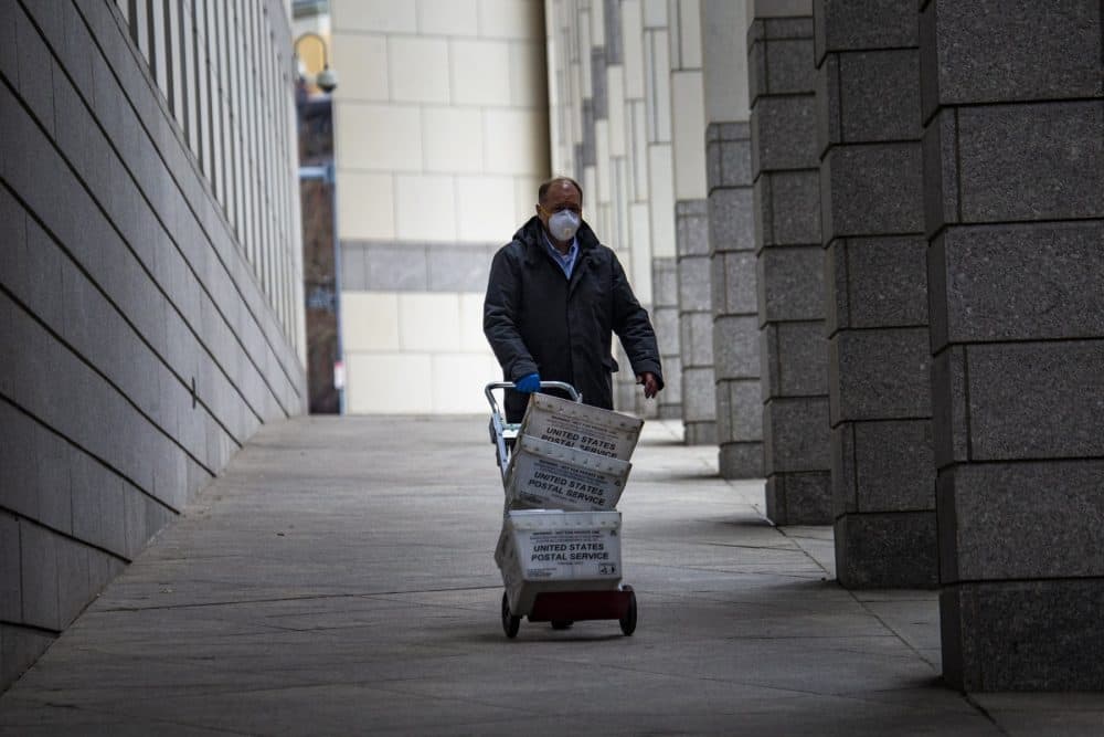 A mail carrier wityh a mask walks through the Edward Brooke Courthouse Plaza. (Jesse Costa/WBUR)