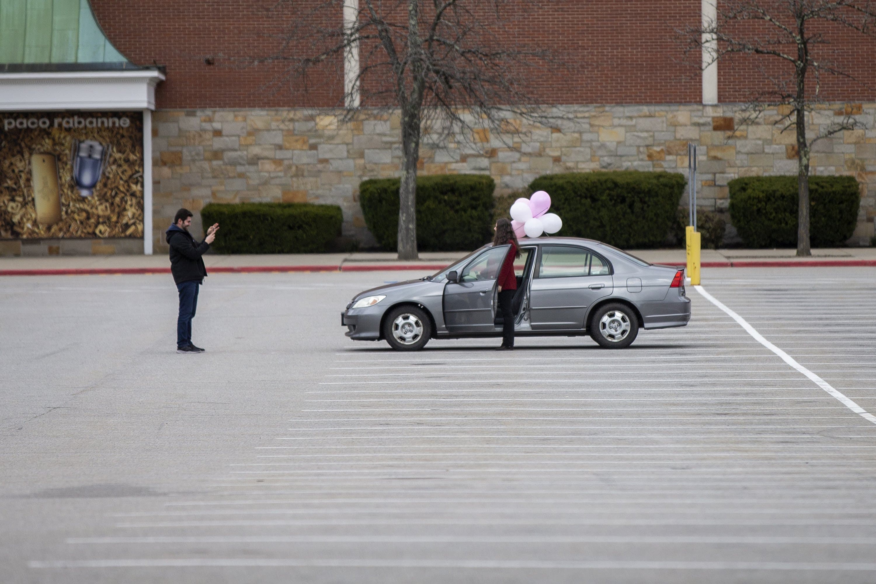 Aykut Turkoglu and his wife Sevil celebrate owning her first car by taking a photo in the empty Burlington Mall parking lot. (Jesse Costa/WBUR)
