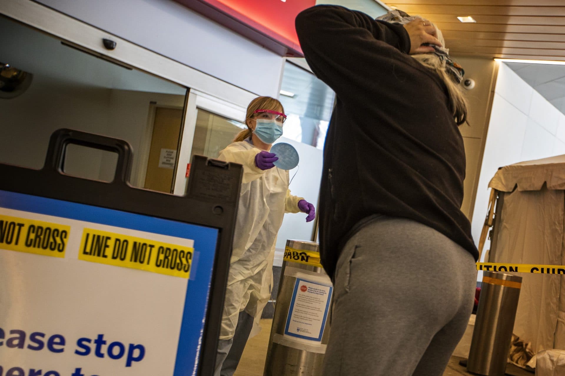 March 27: A health care worker hands a mask to someone wanting to be tested for COVID-19 at a testing tent at Brigham and Women’s Hospital. (Jesse Costa/WBUR)