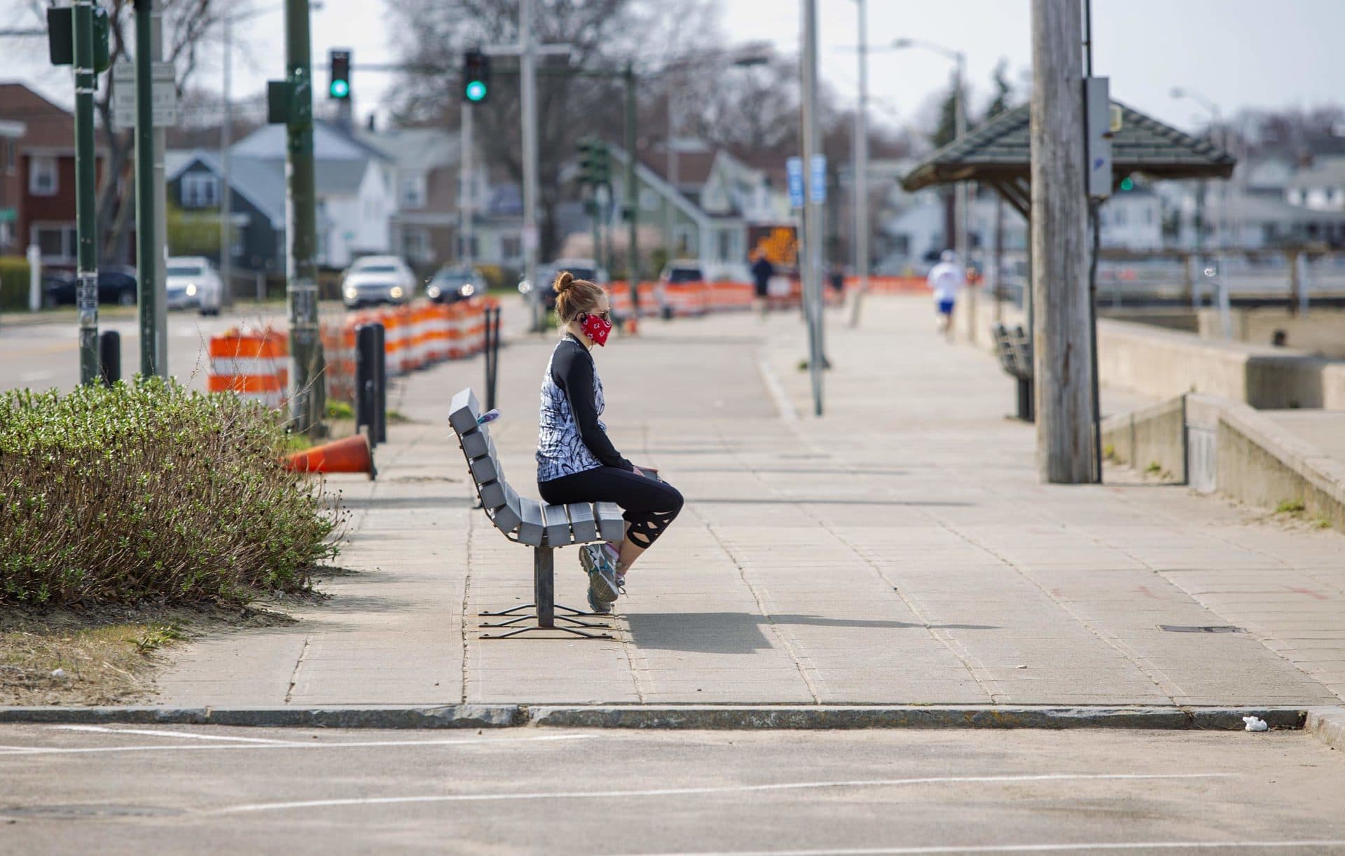 April 7: A woman wearing a mask looks out to sea across Wollaston Beach in Quincy. (Robin Lubbock/WBUR)