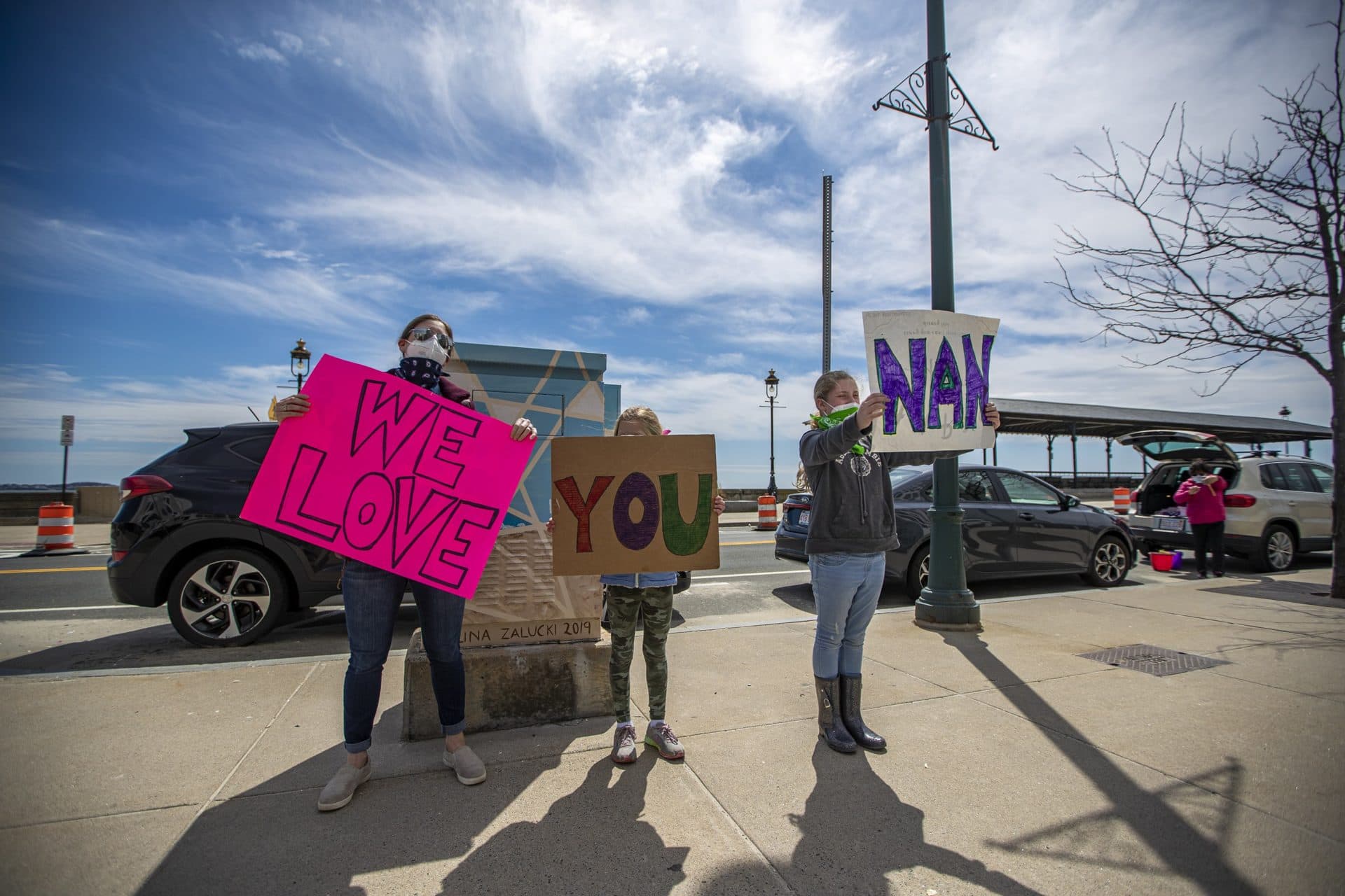 April 14: Jess, Gabby and Frankie Iovanna of Duxbury show signs to their grandmother Nancy as she looks out the window of her room at the Jack Satter House in Revere. (Jesse Costa/WBUR)