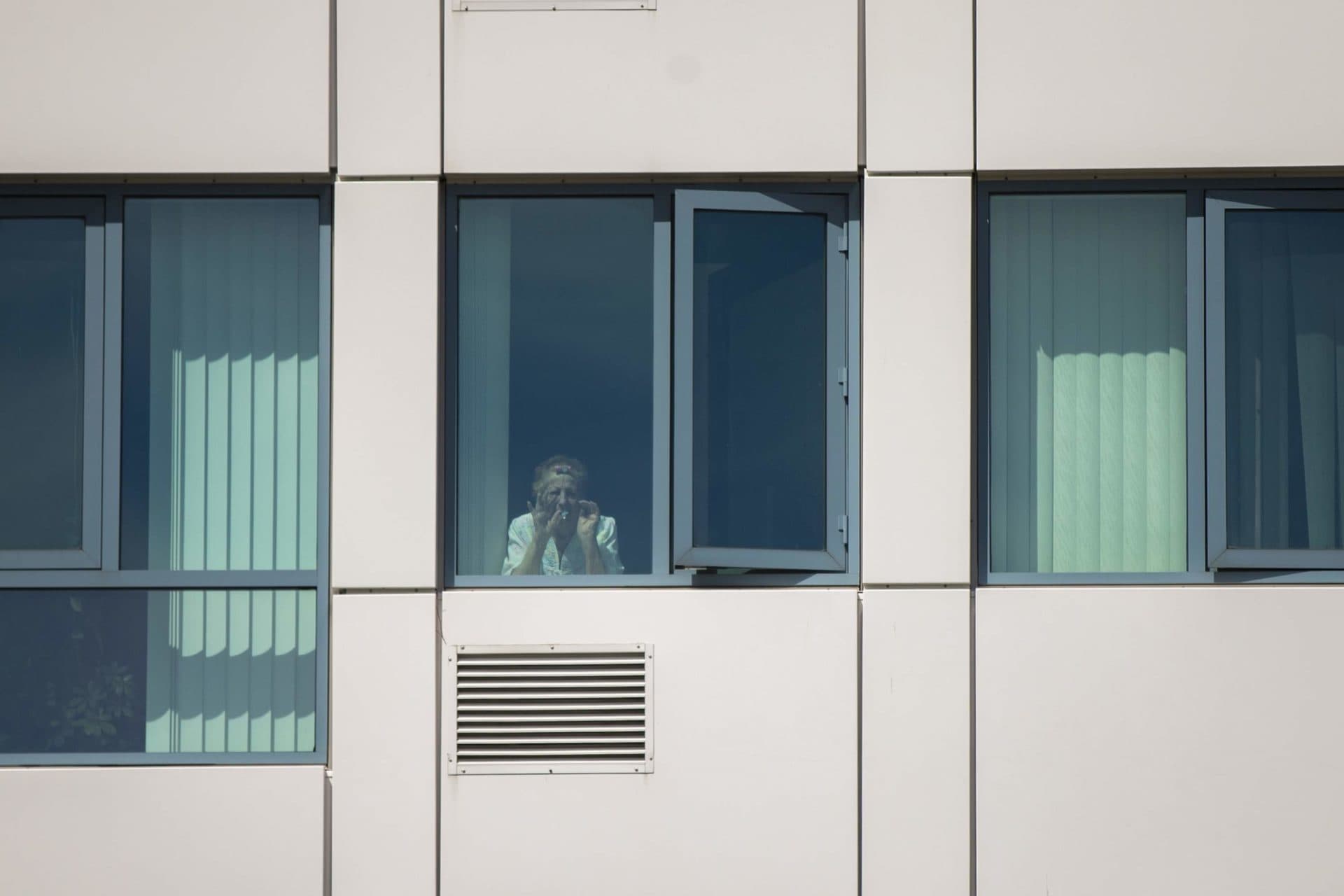 April 14: Nancy Iovanna waves to her family on Revere Beach Parkway from her room at the Jack Satter House. (Jesse Costa/WBUR)