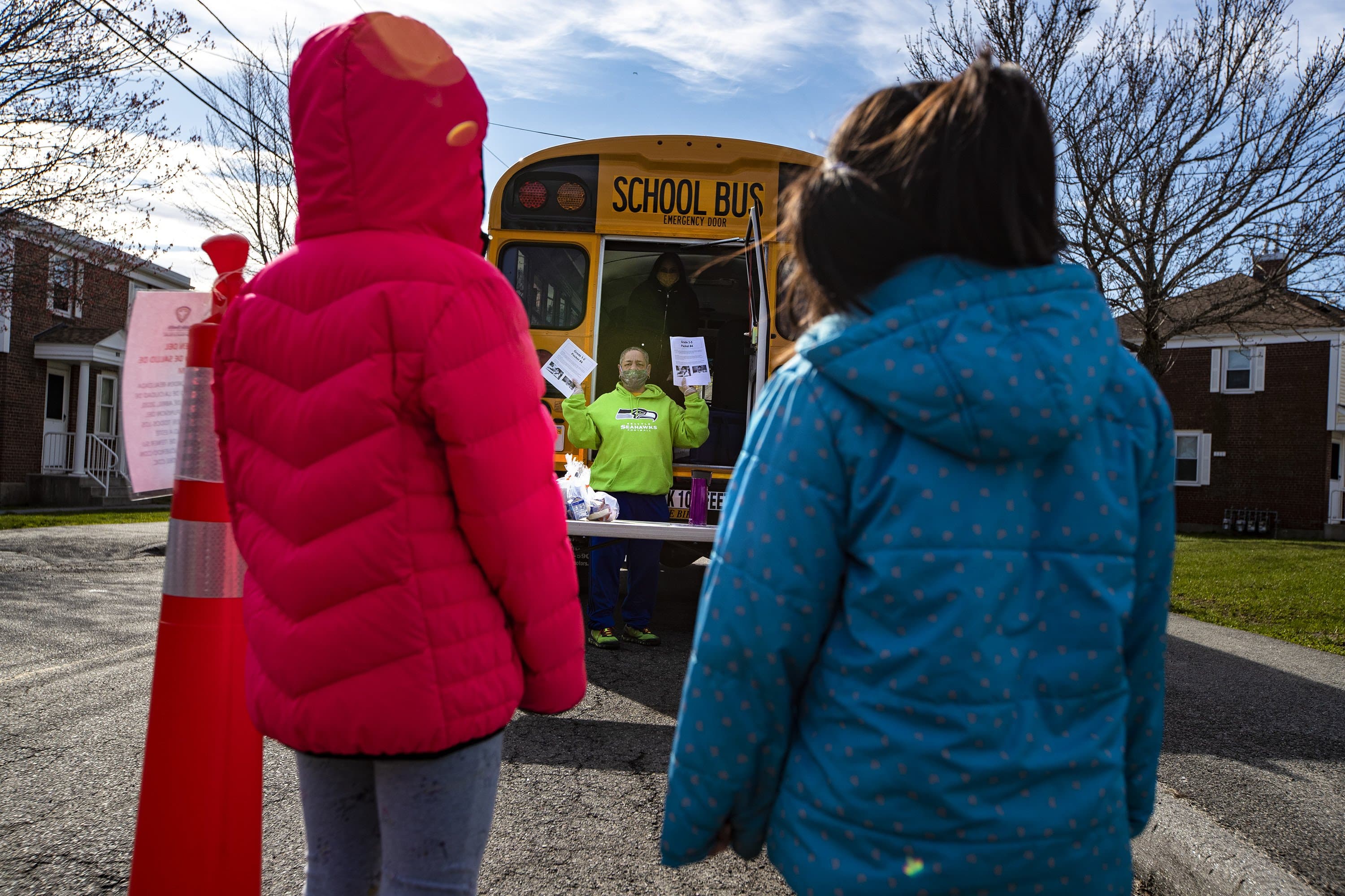 Two students wait as physical education teacher Evelyn Oquendo holds up learning packets, asking how many they will need for the household, for children to do school work online. Salem Public Schools is delivering "grab-and-go" style breakfast and lunch to all children under the age of 18 at designated areas around the city. (Jesse Costa/WBUR)