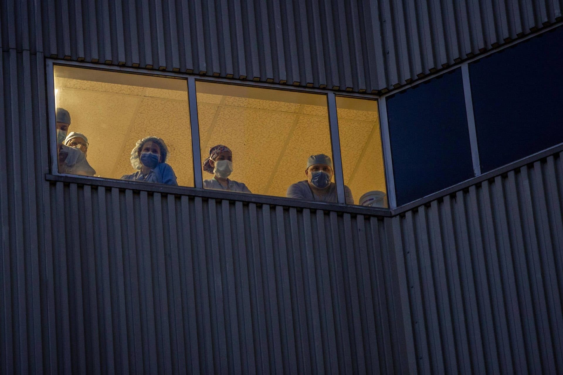 April 15: Medical staff watch from an upper floor window of Tufts Medical Center as a line of Boston emergency vehicles, with lights flashing and horns blaring in support of health care workers, drives by. (Robin Lubbock/WBUR)