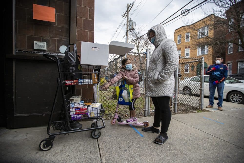 A young girl points out fruit snacks on a cart to her mother as they wait for a food donation from the Salvation Army in Chelsea. (Jesse Costa/WBUR)