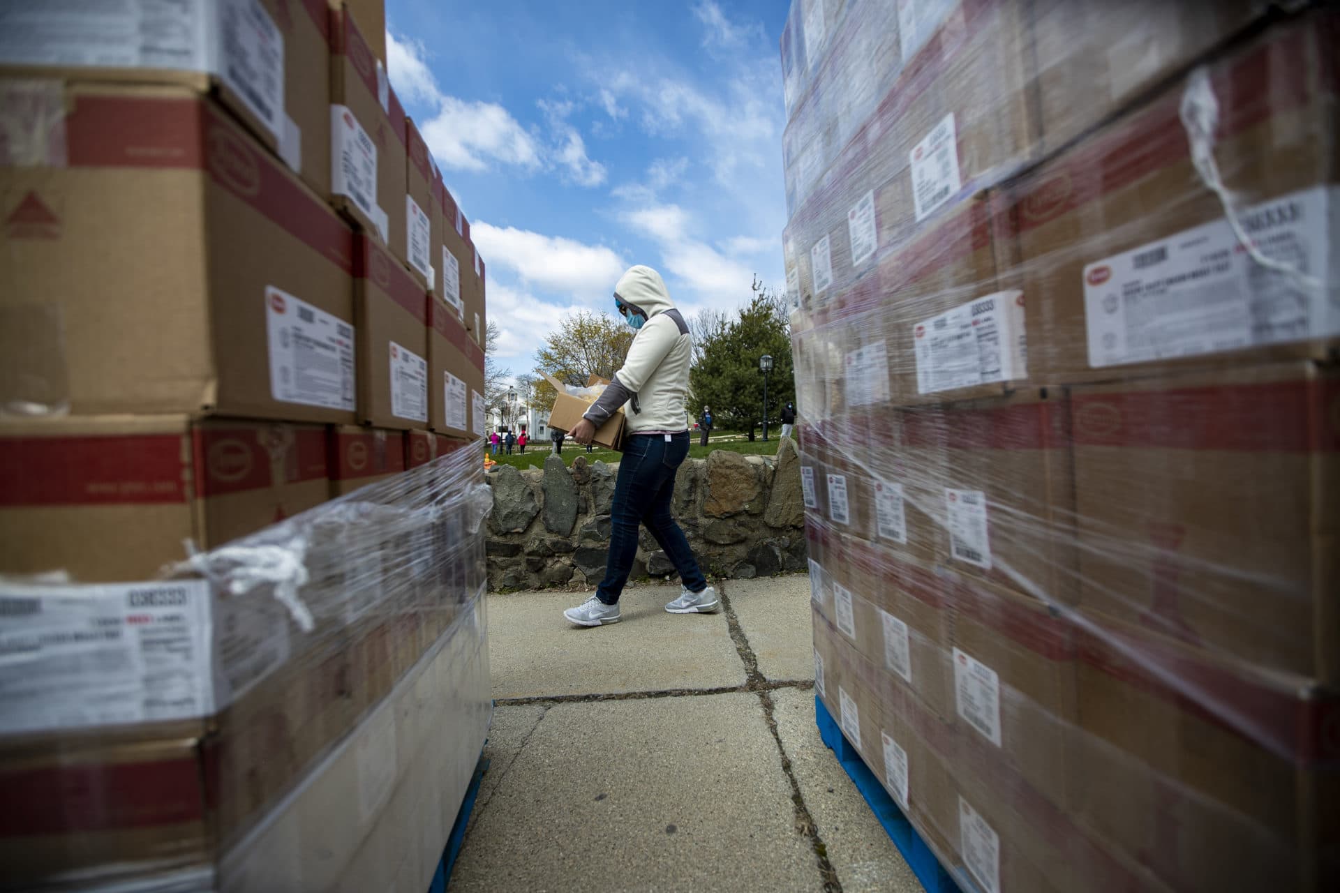 A Chelsea resident is seen carrying a box of food supplies as she passes two pallets of donated breaded chicken patties for a pop-up food pantry at Washington Park. (Jesse Costa/WBUR)