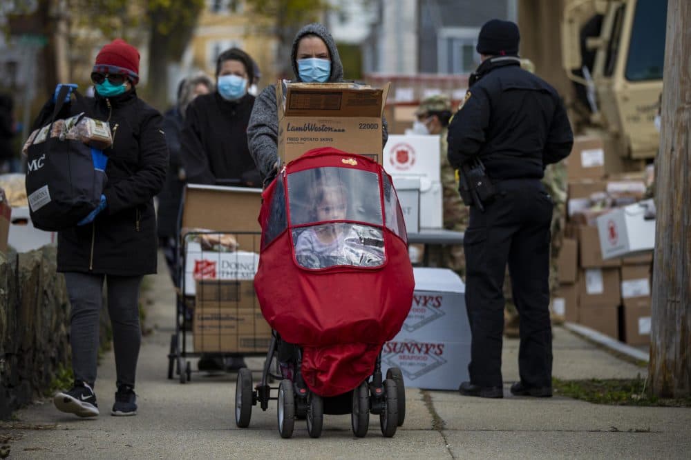 A woman wheeling a carriage with her young daughter walks away with food supplies from a pop-up food pantry at Washington Park in Chelsea. (Jesse Costa/WBUR)