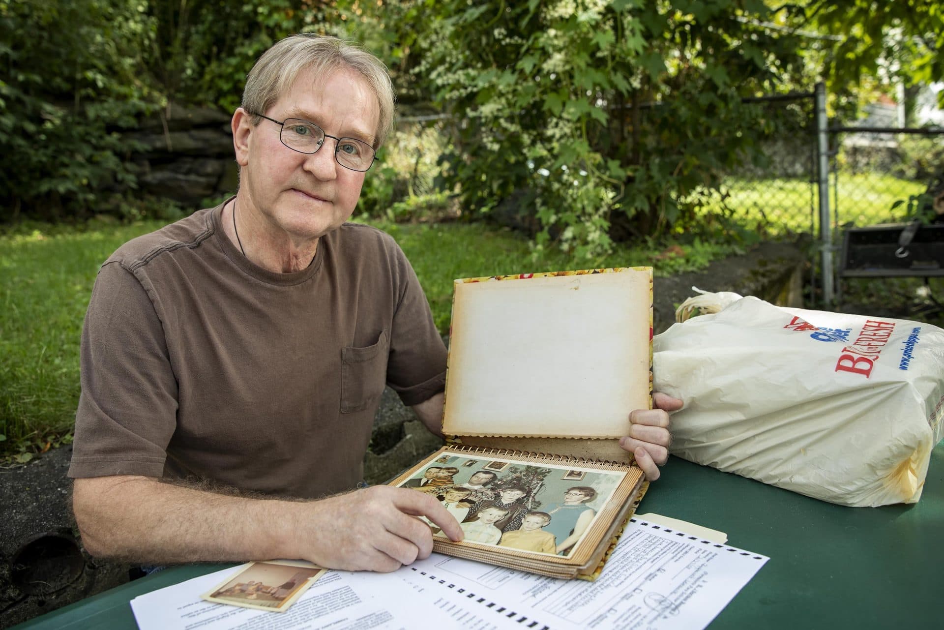 At his home in Worcester, Mario Lemanski holds a family photo album that sits atop paperwork regarding his brother's death. (Robin Lubbock/WBUR)