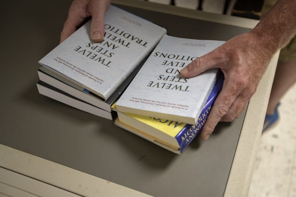 A man sets out various books on a table for Alcoholics Anonymous members to read for a meeting at St. Patrick’s Church in Falmouth, Mass. (Jesse Costa/WBUR)