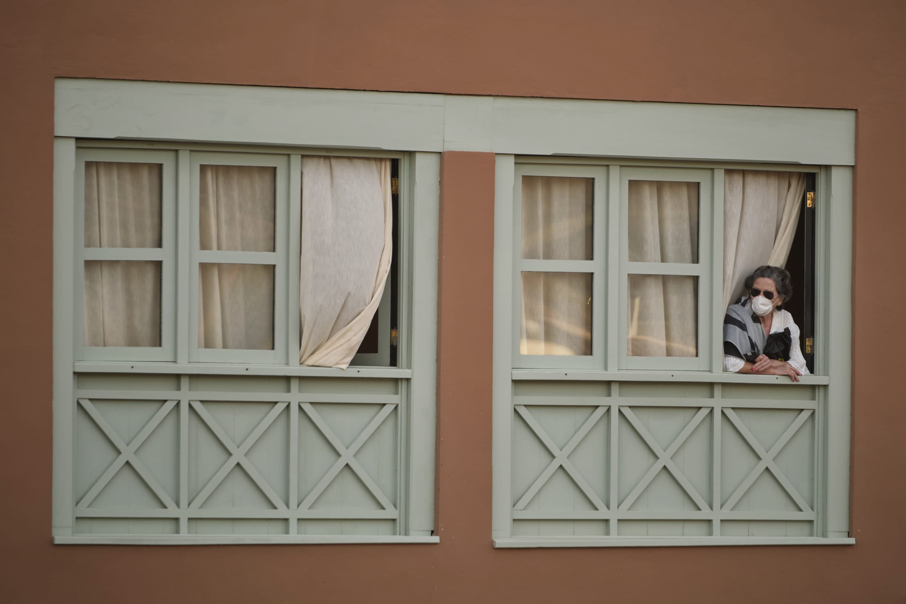 A woman looks out of a window at the H10 Costa Adeje Palace hotel in La Caleta, in the Canary Island of Tenerife, Spain, Feb. 26, 2020. (AP Photo)