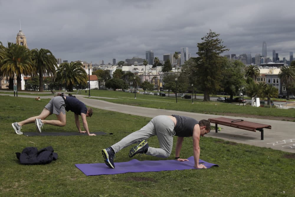 Two men keep their distance for coronavirus concerns while using a phone app to do a full body weight workout at Mission Dolores Park in San Francisco on Tuesday. (Jeff Chiu/AP)