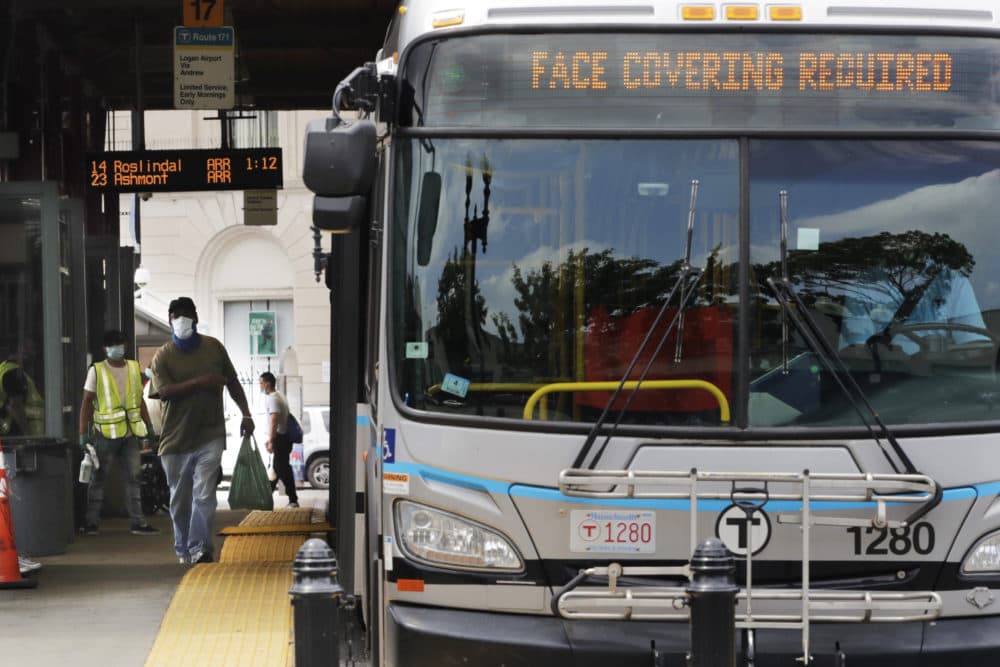 A man, wearing a protective face mask, rushes to catch his bus at Dudley Station in Nubian Square on June 24, 2020, in Boston. (Charles Krupa/AP)
