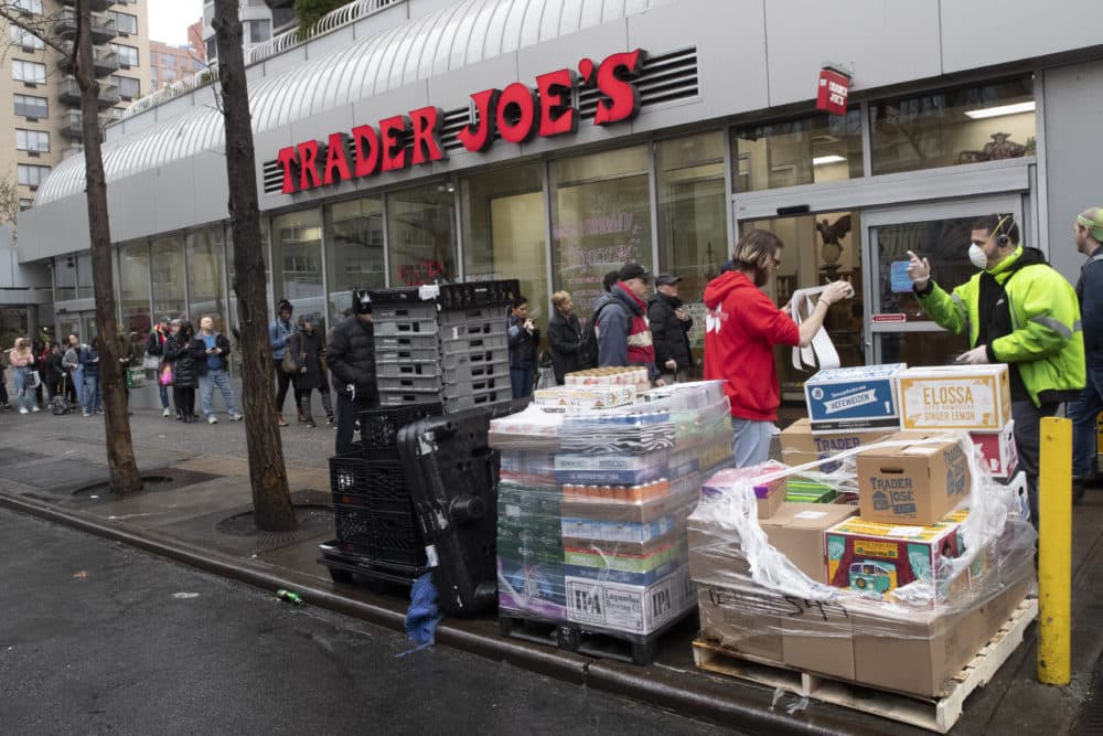 A Trader Joe's employee, second from right, receives groceries from a delivery man, right, as customers line up to enter the store, Friday. (Mary Altaffer/AP)
