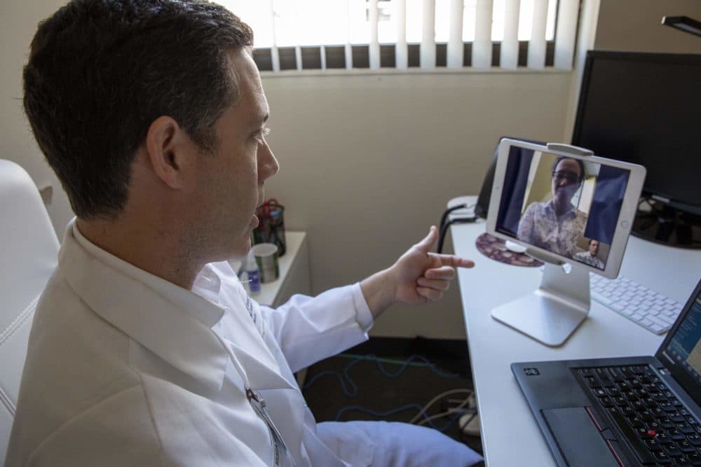 The coronavirus pandemic has prompted more people in Massachusetts to turn to telemedicine. Here, Dr. Philip Ciampa from the Atrius Health innovation center (left) talks with a colleague (at the top of the screen), in a demonstration of a &quot;virtual visit.&quot; (Robin Lubbock/WBUR)