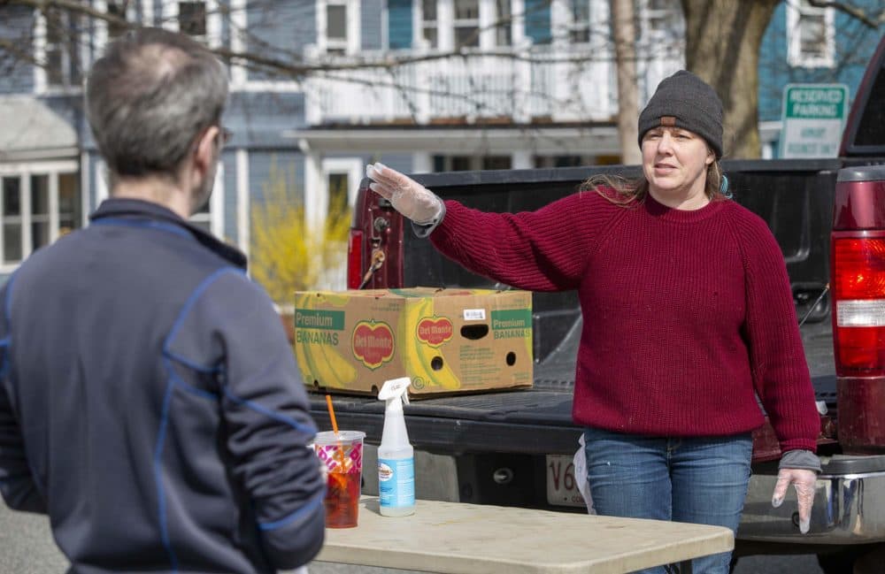 Farmer Kate Stillman gestures with a safely gloved hand, as she talks to a customer at her farm stand at the Somerville Armory. (Robin Lubbock/WBUR)