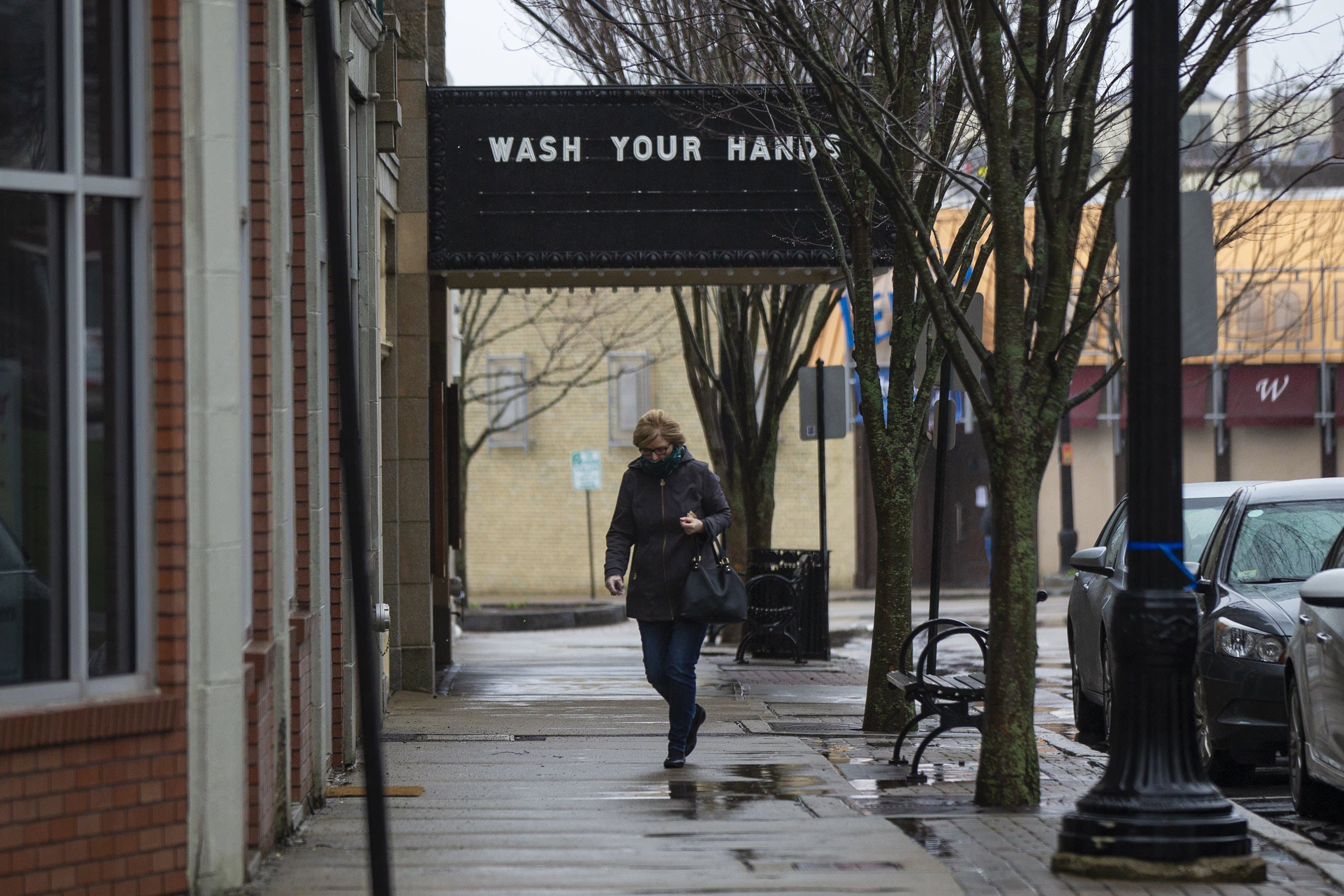 A woman walks past a closed Norwood Cinema where the marquee reads "Wash your hands." (Jesse Costa/WBUR)