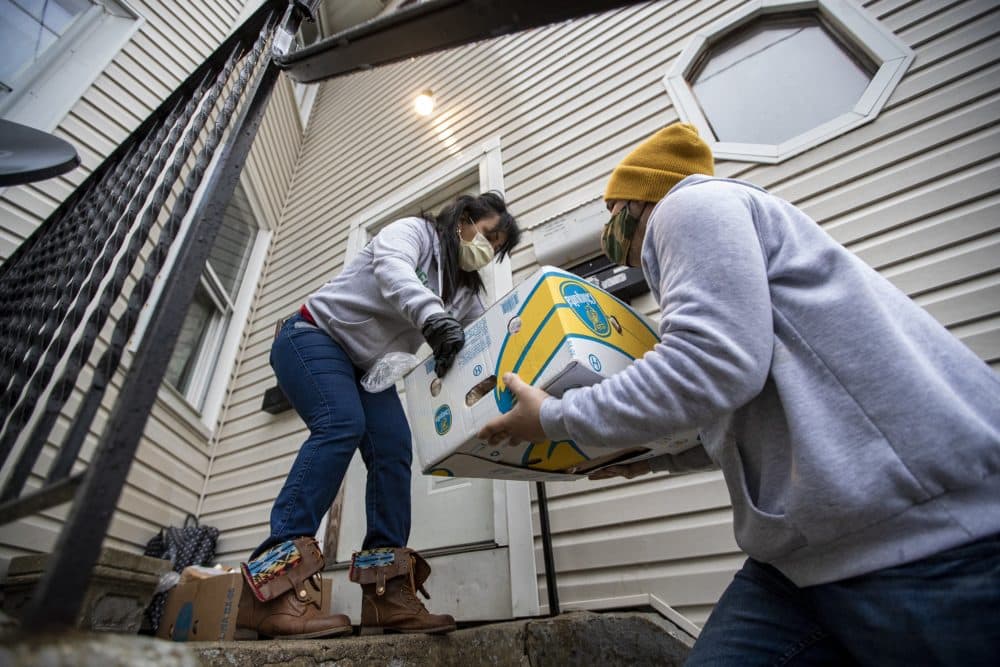 Reymer Pineda hands a box of donated food to Gladys Vega to leave on the front porch of the house. All members of the household have contracted COVID-19, and will come out after Vega calls them to let them know. (Jesse Costa/WBUR)