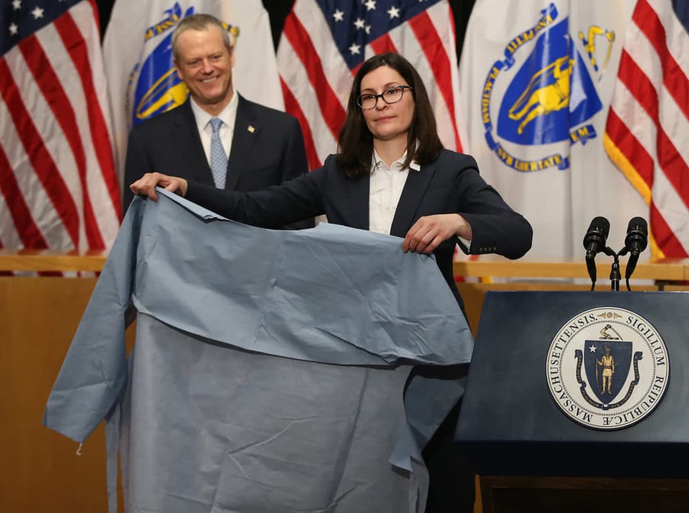 Gov. Charlie Baker looks on as Brenna Schneider, CEO of 99Degrees, shows off a surgical isolation gown during a media availability at the State House to discuss updates relating to COVID-19 on April 13, 2020. (Nancy Lane/MediaNews Group/Boston Herald)