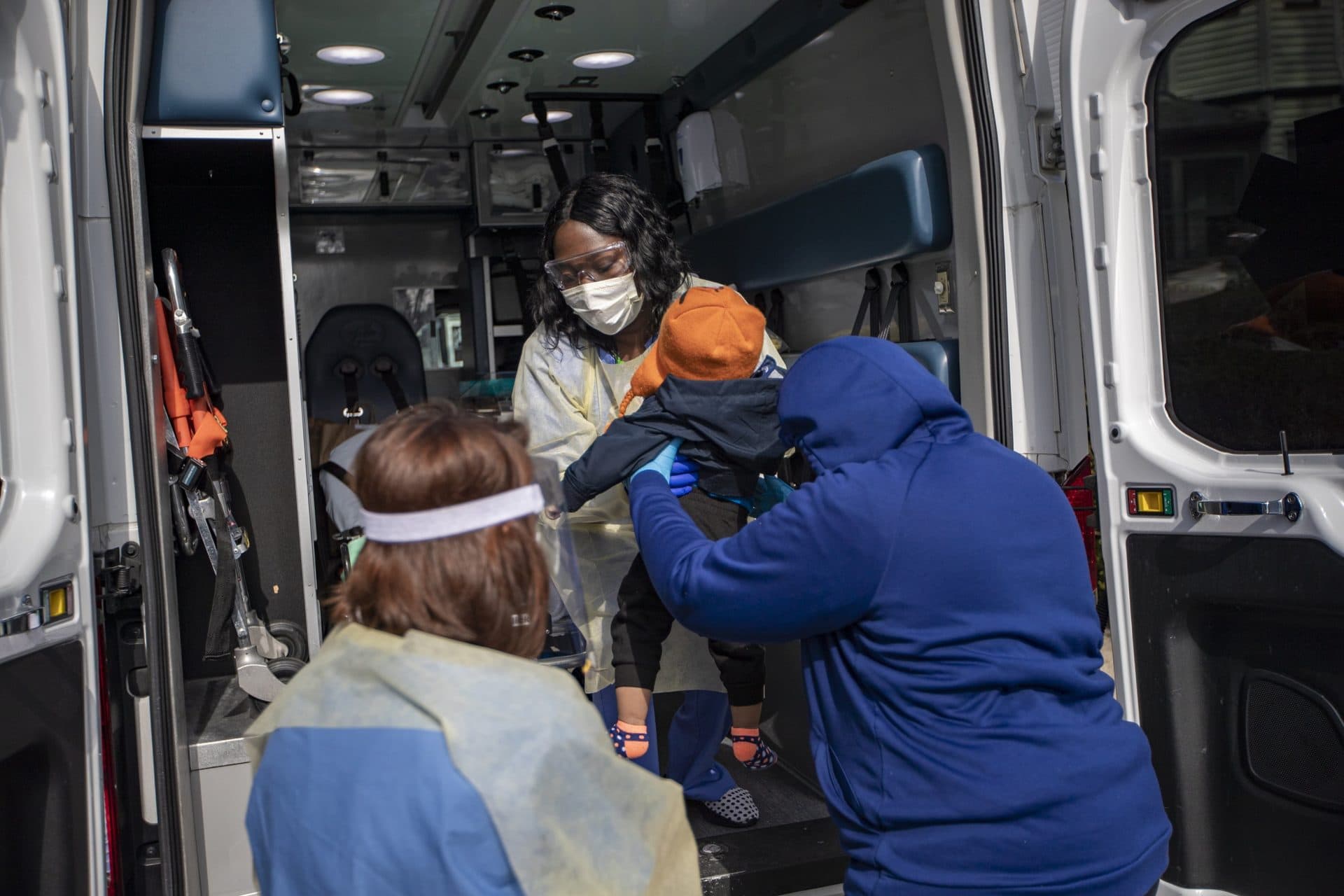 BMC nurse Priscilla Stout takes a baby from his aunt to be examined in the back of the ambulance in Dorchester. (Jesse Costa/WBUR)