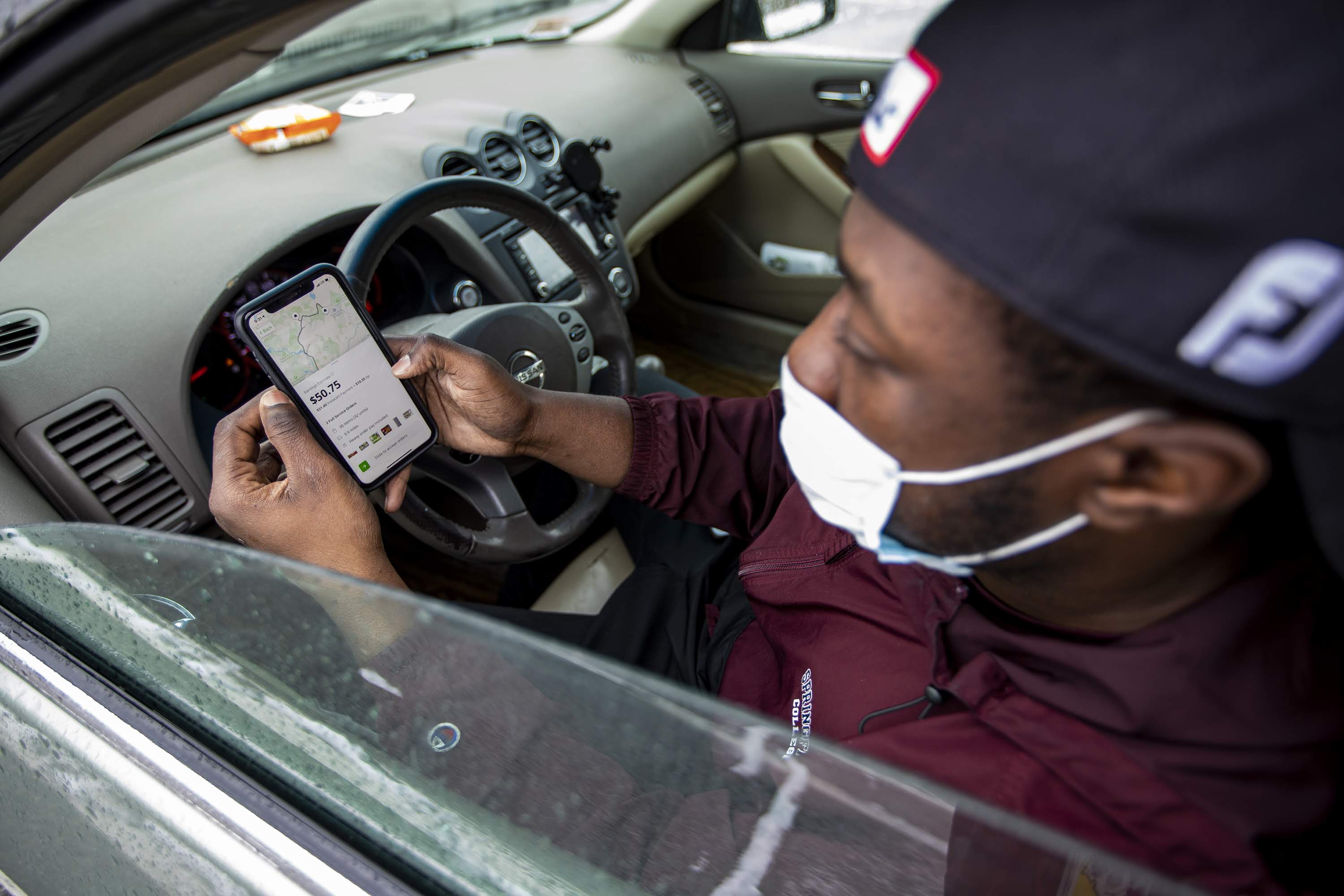 In his car at Costco in Dedham, Instacart shopper Shamar Martin looks at a double order on the Instacart app. (Jesse Costa/WBUR)