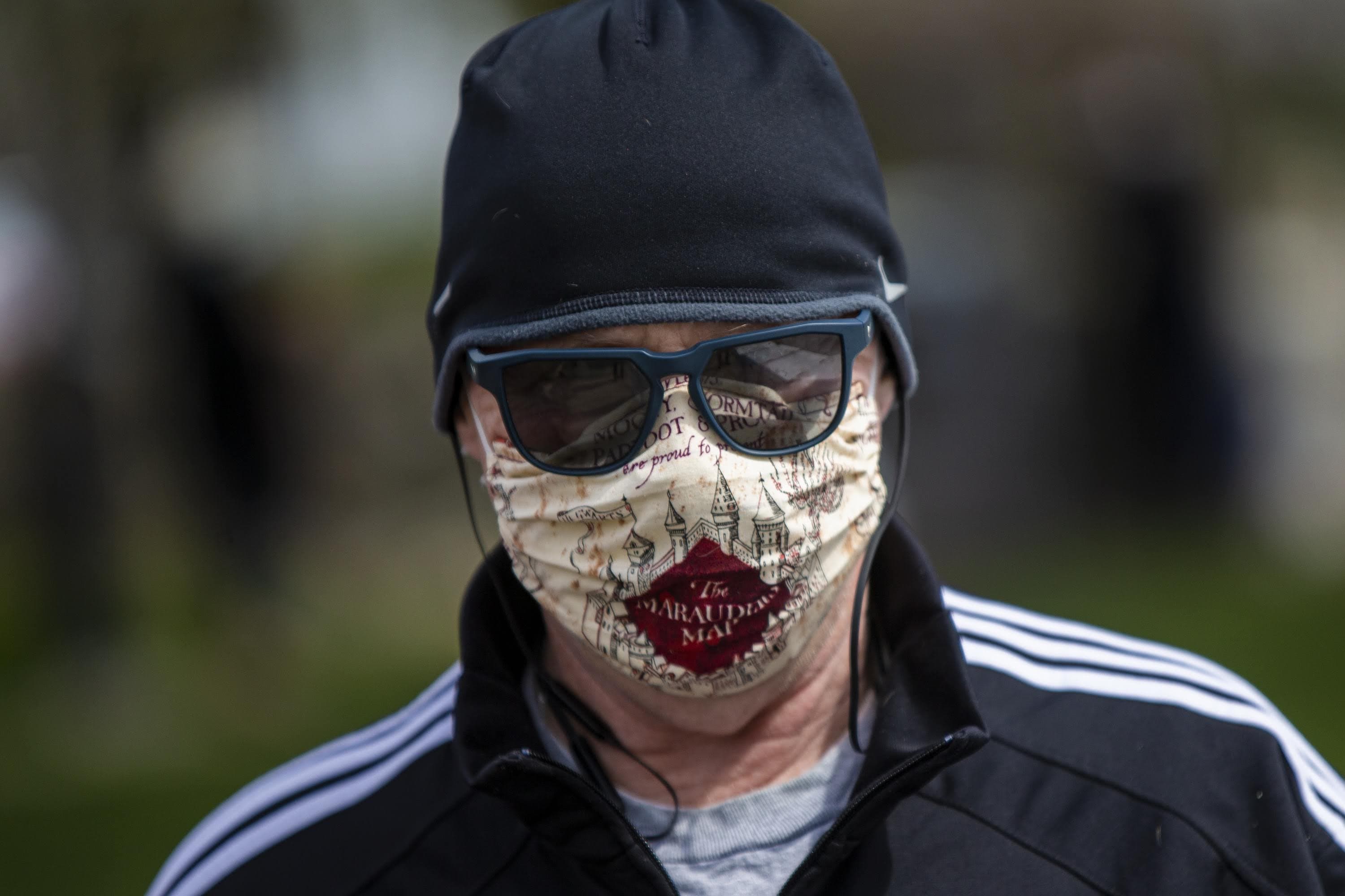 A man walking his dog past Washington Park in Chelsea wearing a Harry Potter Marauder’s Map mask during the COVID-19 pandemic. (Jesse Costa/WBUR)