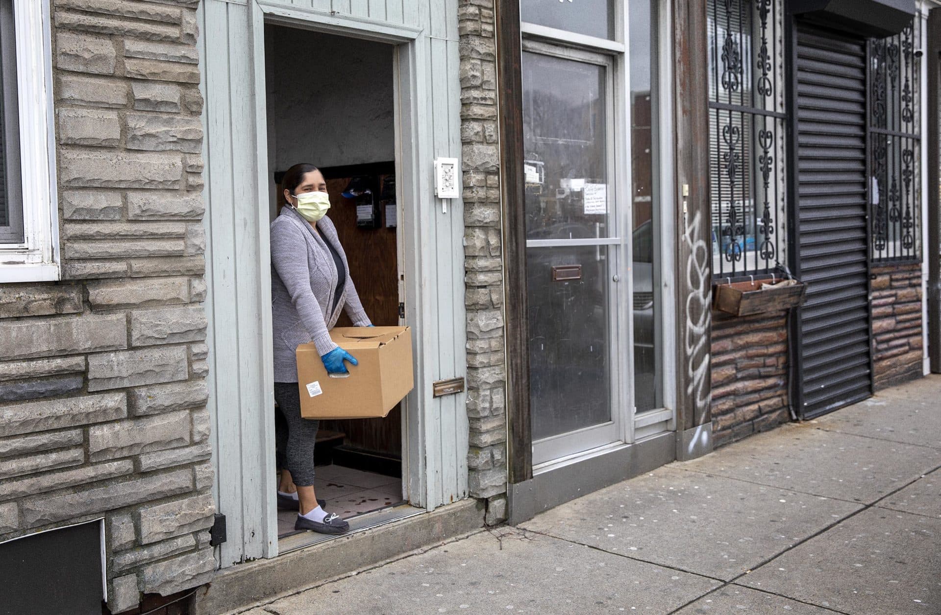 Angelica, who is isolating herself after testing positive for COVID-19, collects the Centro Presente food delivery from her doorstep. (Robin Lubbock/WBUR)