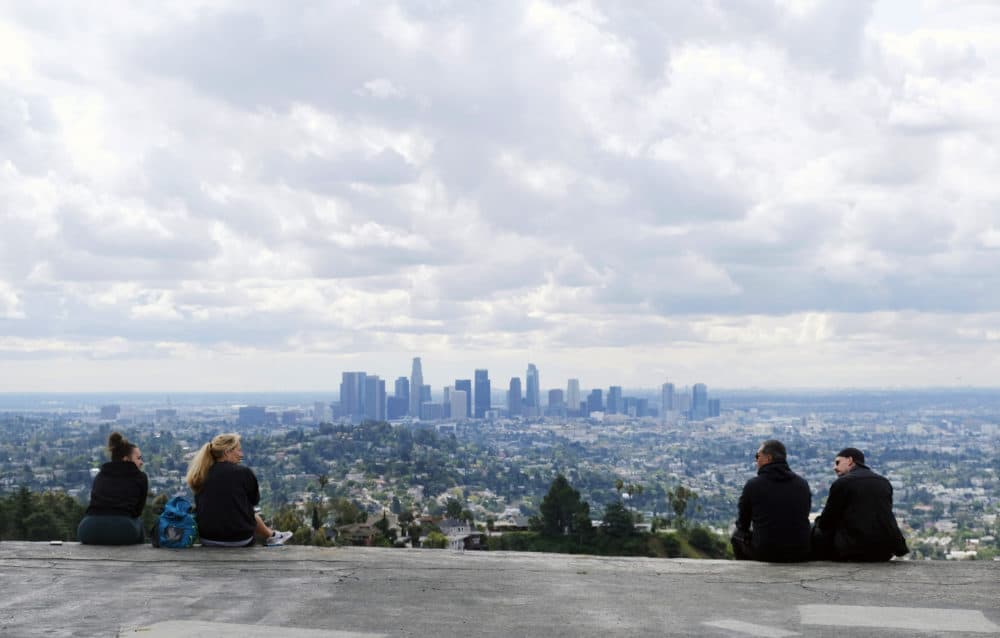 In this Friday, March 20, 2020 file photo, two pairs of hikers maintain social distance as they mingle at Vista View Point in Griffith Park in Los Angeles as storm clouds pass through. Southern Californians are seeing excellent air quality, resulting from business closures during the coronavirus pandemic and recent rain. (Chris Pizzello/AP)