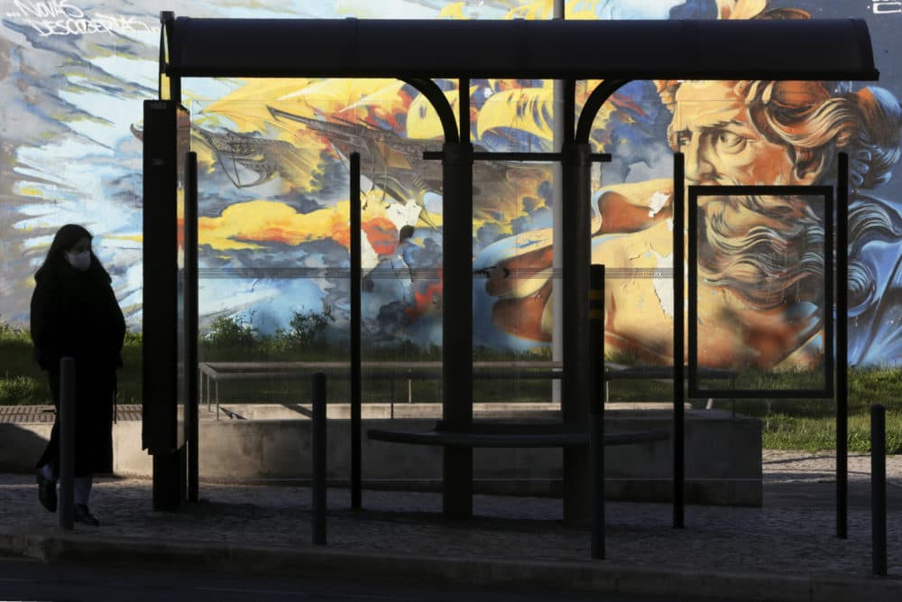 A woman wearing a face mask walks by a bus stop in Lisbon, Wednesday, April 22, 2020. Portugal is in the fifth week of a government declared state of emergency due to the coronavirus pandemic. (Armando Franca/AP)