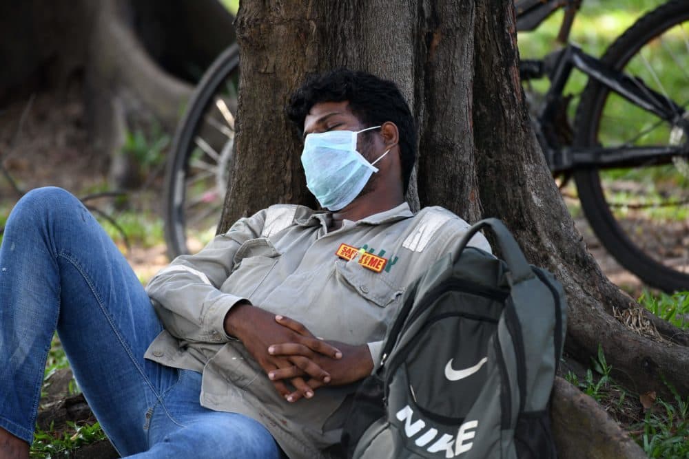 A man wearing a face mask and a tag that reads &quot;Safety starts with me&quot; takes a nap in Singapore on April 15, 2020. (Roslan Rahman/AFP/Getty Images)