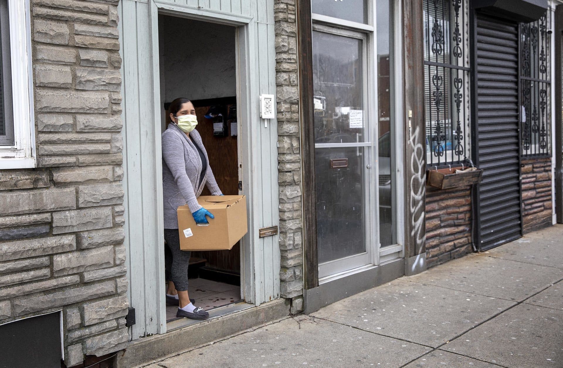Angélica, quien se aisló luego de salir positivo en la prueba de COVID-19, recoge la caja de comida de Centro Presente en la entrada de su casa. (Robin Lubbock/WBUR)