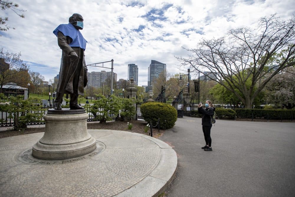 A woman takes a photo of a masked statue of Edward Everett in the Boston Public Garden. (Jesse Costa/WBUR)