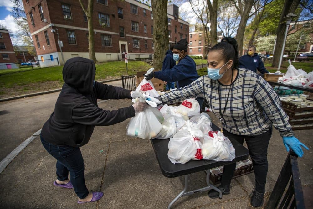 Cherry Gomez (foreground), Bonnie Jones and Dianne Horne, all BHA employees, hand out meals at the Mary Ellen McCormack complex in South Boston. The city has distributed more than 1.1 million youth meals and about 70,000 adult meals at more than 90 such sites around the city during the pandemic. (Jesse Costa/WBUR)