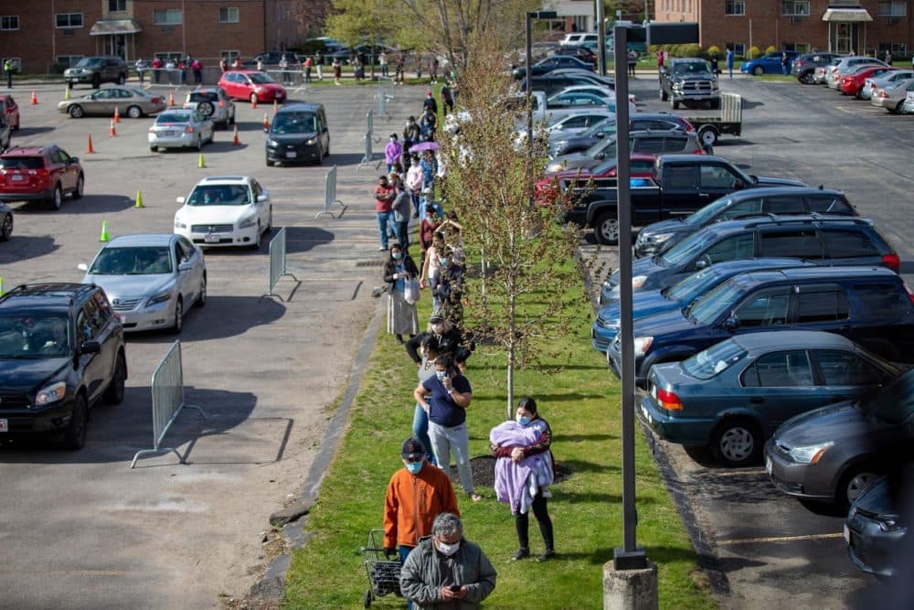 The line for food extends out of the parking lot and down Pond Street at a food pantry at St. Mary Parish in Waltham. People lined up on foot and in their vehicles at St. Mary Parish in Waltham where nearly 3,000 bags of groceries were passed out to families in need. (Jesse Costa/WBUR)
