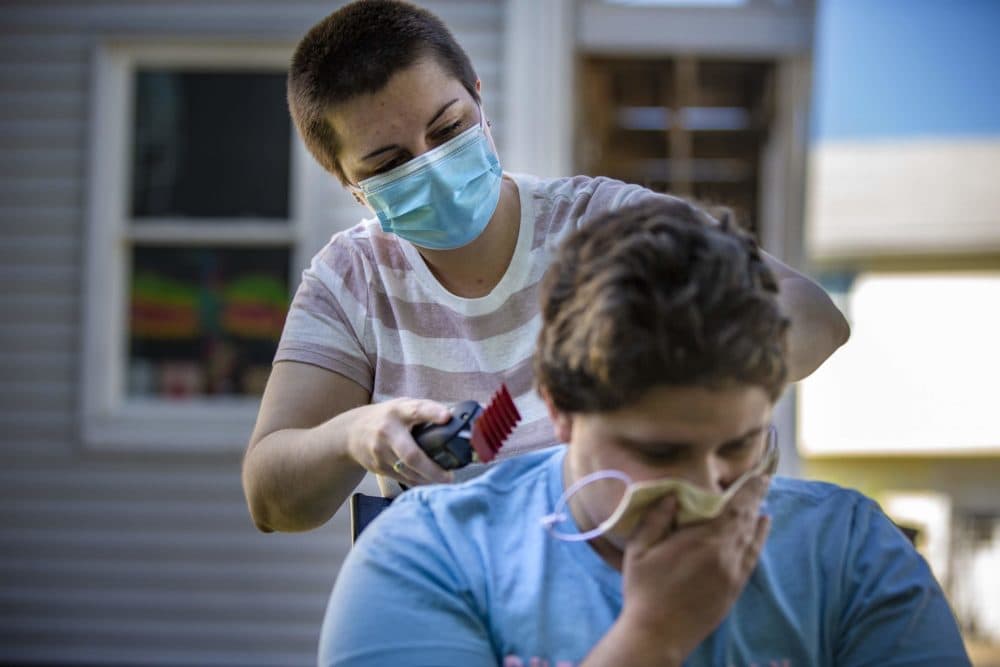 Neighbor Lauren Keisling trims the hair of Ryley Copans in their backyard with a brand new pair of clippers. (Jesse Costa/WBUR)